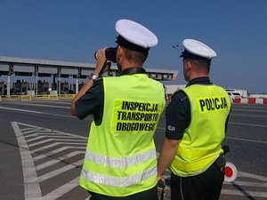 Funkcjonariusz Inspekcji Transportu Drogowego oraz policjant obserwują nadjeżdżające pojazdy.