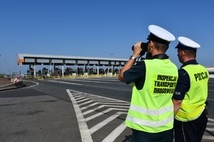 Policjant i inspektor transportu drogowego obserwują nadjeżdżające pojazdy.