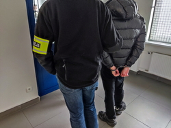 Na zdjęciu policjant stoi z zatrzymanym w policyjnym areszcie.