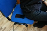 mężczyzna siedzi na krześle, widać telefon który wypadł mu z kieszeni