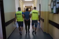 Policjanci w kamizelkach z napisem policja prowadzą podejrzanego