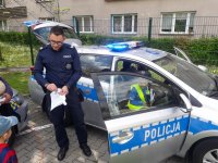 Policjant przy radiowozie, na siedzeniu pasażera mały chłopiec w policyjnej czapce