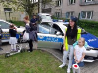Cywile na tle radiowozu - kobieta w czapce policyjnej z małą dziewczynką