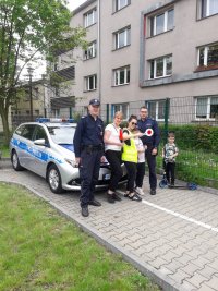 Dwaj umundurowani policjanci i cywile na tle radiowozu.