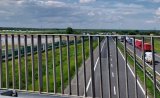 Przez barierki wiaduktu autostradowego widzimy stające na autostradzie dwa szeregi pojazdów.