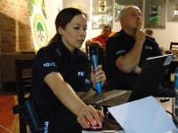 Policjanta na pierwszym planie, siedzi przy komputerze.