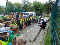 Dzieci słuchają wykładu policjanta kucającego i tłumaczącego...