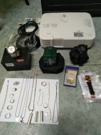 Od góry rzutnik multimedialny, niżej zegarki a najniżej pierścionki, łańcuszki - złota biżuteria.