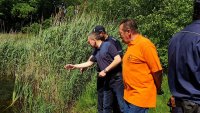 Mężczyźni po cywilnemu i policjant pochylają się i patrzą w stronę jeziora
