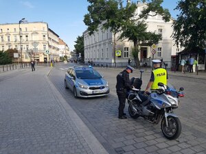 Policjanci przy radiowozie i motocyklu służbowym patrzą na ruch....