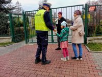 Policjant wręcza dziecku i opiekunom upominek