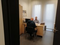 Policjant po cywilnemu przy biurku przesłuchuje podejrzanego.