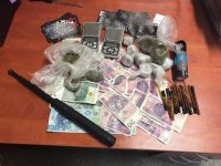 Na stole wyłożone: pieniądze, narkotyki w woreczkach, wagi, pałka teleskopowa.