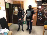 Policjant w kominiarce po cywilnemu pilnuje stojącego obok zatrzymanego.