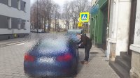 Młody mężczyzna pochyla się przy drzwiach nieoznakowanego radiowozu, w tle nieprawidłowo zaparkowany renault.