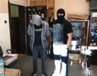 Policjant w kominiarce pilnuje zatrzymanego z kapturem na głowie