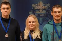 Dwaj policjanci i policjantka po cywilnemu na tle planszy z logo policja gliwice.