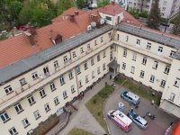 Budynek szpitala i dzieciniec na którym stoja policyjny radiowóz, motocykl i karetka pogotowia
