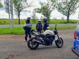 Policyjna kontrola motocyklisty. Stoi policjant i dwóch motocyklistów. Na pierwszym planie motocykl.