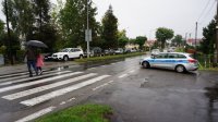 Policyjny radiowóz po prawej stronie. Po lewej ulica a w tle - szkoła.
