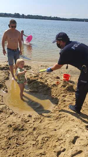 Policjant na plaży pzekazuje dziecku prezent.