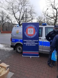 Policjyjny radiowóz a przed nim plansza reklamowa sanepidu Gliwice.