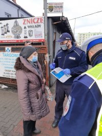 Dwaj policjanci rozmawiaja z kobietą przy targowisku.