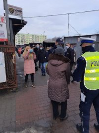 Dwaj policjanci rozmawiaja z kobietą przy targowisku.