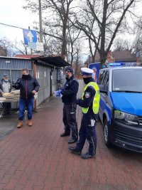 Dwaj policjanci i radiowóz przed wejściem na targowisko miejskie.