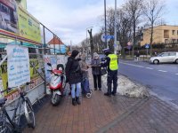 Policjant rozmawia z ludźmi na chodniku przy targu.