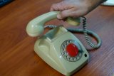 Ręka podnosi słuchawkę starego telefonu z okragła tarczą numeryczną.