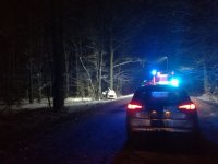 Na fotografii - leśna droga, wieczór, radiwozóz na pierwszym planie w oddali po lewej stronie poza drogą samócho osobowy rozbity na drzewie.