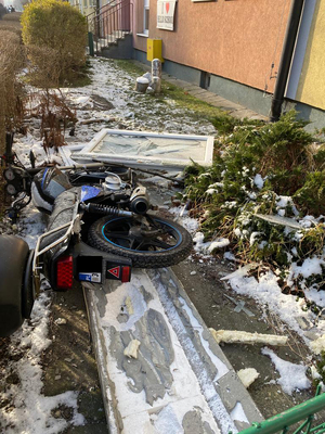Porozrzucane fragmentu okien, elewacji, przewrócony motorower.