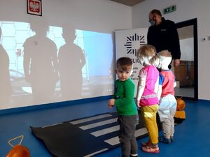 Policjant i dzieci przed zainscenicowanym w klasie przedszkolnej przejąciem dla pieszych.