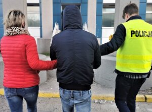 Policjant po prawej i policjantka po lewej prowadzą zatrzymanego.