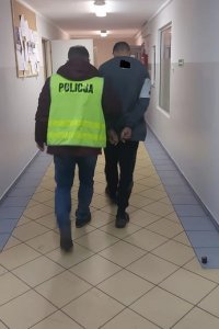 Policjant prowadzi zatrzymanego korytarzem.