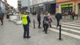 Policjant przed przejściem dla pieszych rozdaje odblaski nadchodzącym osobom.