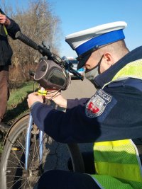 Policjant mocuje na ramie roweru odblaskowy element.
