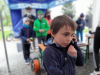 Na pierwszym planie chłopczyk rozmawiający przez telefon, w tle namiot z napisem policja i grypa osób.