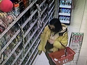 Kobieta w kurtce z kapturem i koszykiem w sklepie drogeryjnym.