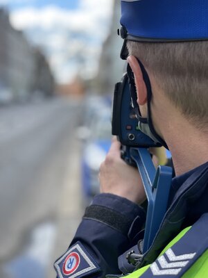 Policjant z miernikiem prędkości skierowanym w stronę trójpasmowej ulicy.