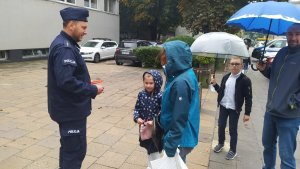 Policjant rozmawia z dziećmi i ich rodzicami przed szkołą.