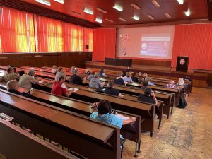 Aula, widzimy ławki a w nich siedzą osoby dorosłe, słuchają wykładu prowadzonego przez policjanta.