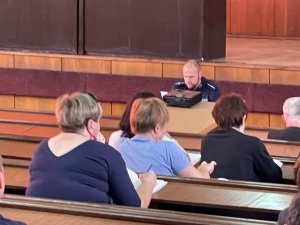 Aula, widzimy ławki a w nich siedzą osoby dorosłe, słuchają wykładu prowadzonego przez policjanta.