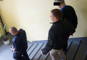 Policjanci prowadzą po schodach zatrzymanego.