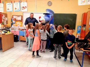 Policjant - dzielnicowy wśród dzieci, obok policyjna maskotka Sznupek.