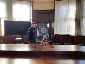 Chłopiec i policjant na tle gabloty z wyeksponowanym sztandarem jednostki.