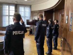 Policjanci składają ślubowanie stojąc w szeregu z uniesionymi prawymi rękami w geście ślubowania.