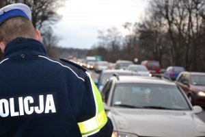 Policjant drogówki, w tle szereg samochodów osobowych w zatorze drogowym.