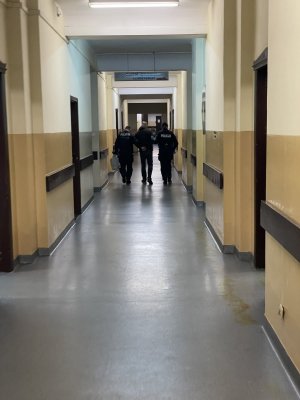 Policjant i policjantka prowadzą korytarzem zatrzymanego.